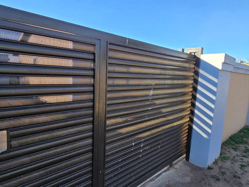 A secure metal sliding gate with a perimeter wall and concrete pillars, providing street-facing access to the property.
