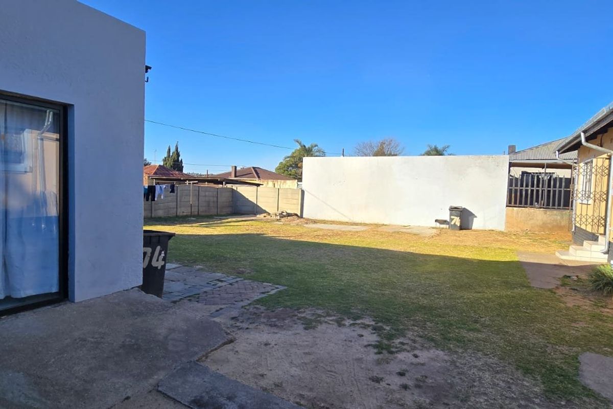 A rear exterior view of the property featuring a lawn, concrete patio area, and boundary walls.