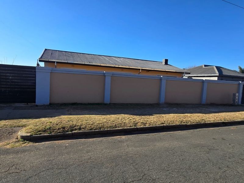 Street view of the property showing the perimeter wall, metal gate, and roofline from the road.