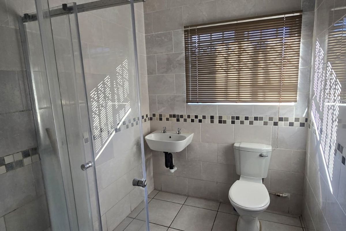 A clean, modern bathroom featuring a glass-enclosed shower, wall-mounted basin, and neutral tiled finishes throughout.