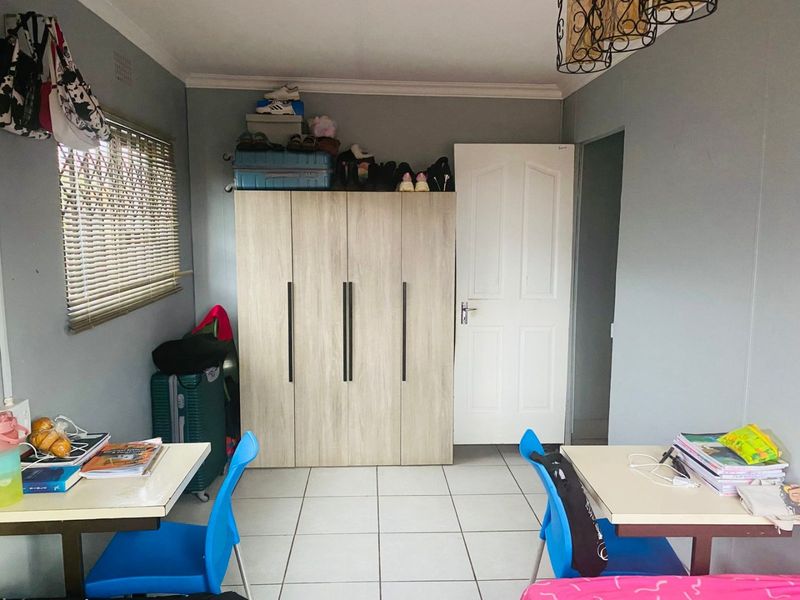 A functional bedroom featuring tiled flooring, a built-in wardrobe, and venetian blinds, offering a practical space with neutral wall finishes.