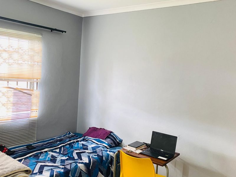 A functional bedroom featuring neutral grey walls, a built-in wardrobe, and natural light provided by a window with fitted venetian blinds.