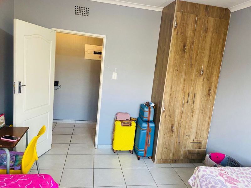 A bedroom featuring tiled flooring and a built-in wooden wardrobe, with an adjacent doorway leading to a utility area.