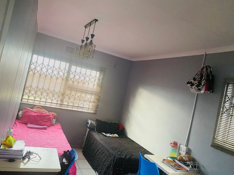 A functional bedroom featuring tiled flooring, a security gate on the window, and a central ceiling light fixture.