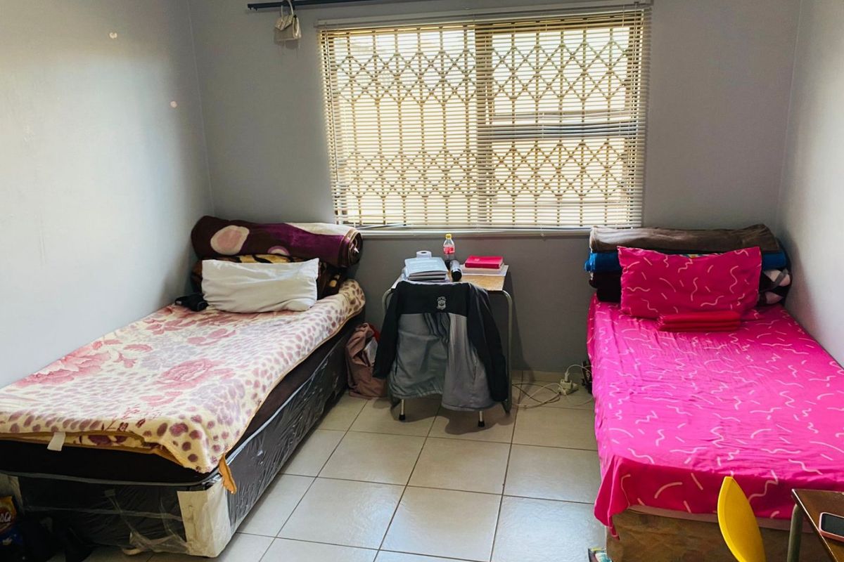 A functional bedroom featuring tiled flooring, a window with security bars, and venetian blinds, providing a practical space for rest.