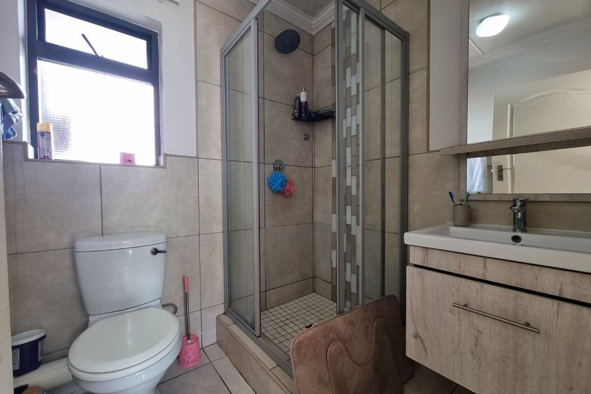 A functional bathroom featuring a shower enclosure, vanity cabinet with basin, and toilet, finished with neutral wall and floor tiles.
