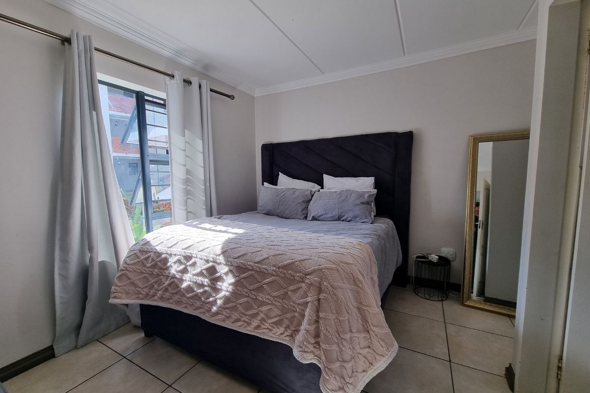A well-maintained bedroom featuring neutral tiled flooring, a large window with aluminium frames, and classic ceiling cornicing.