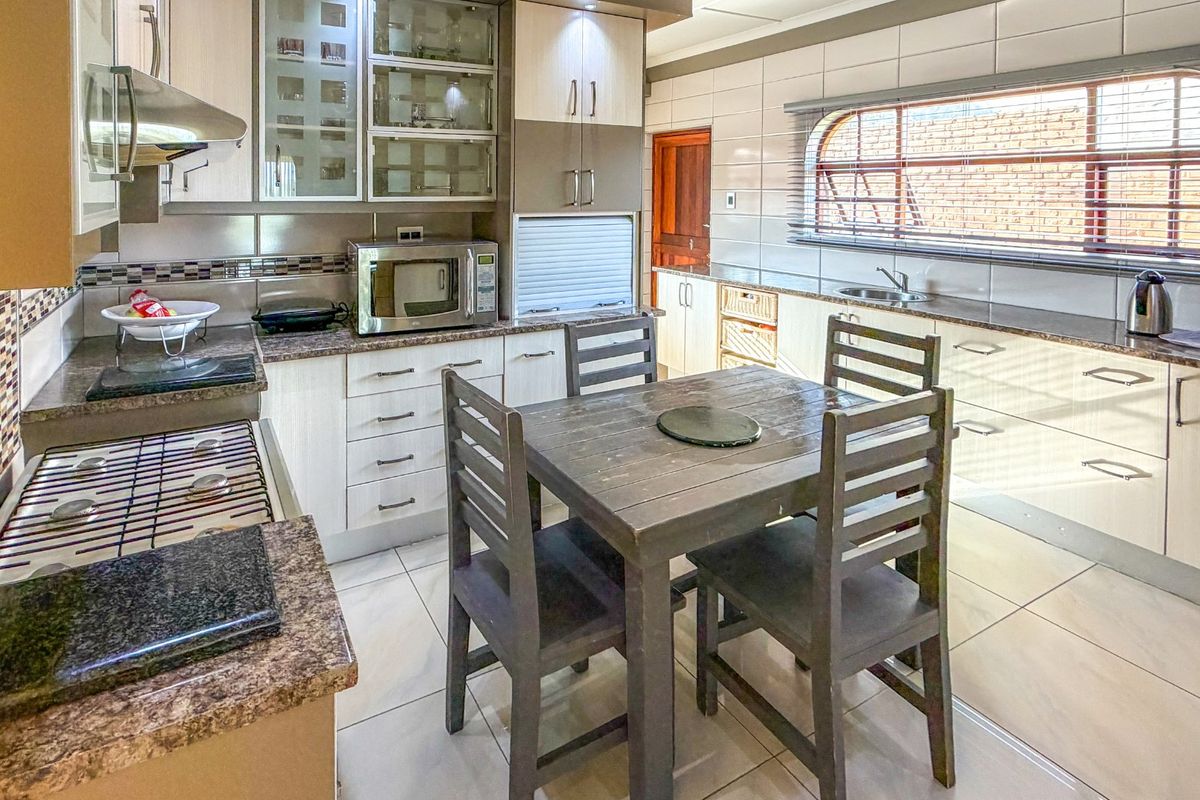 A functional kitchen featuring granite countertops, gas hob, extractor fan, and ample built-in cabinetry with a tiled backsplash and flooring.