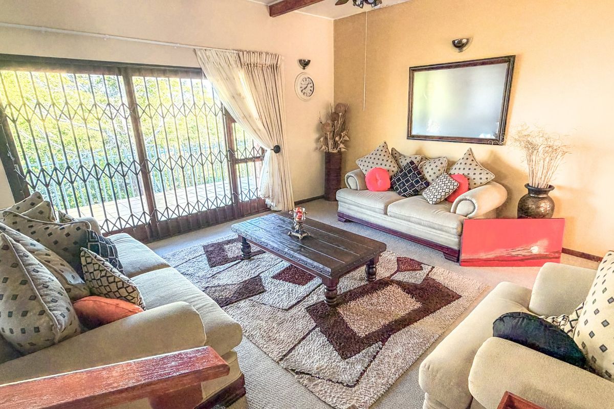 A comfortable living room featuring a large sliding glass door with security gate, exposed ceiling beams, and wall-mounted lighting fixtures.