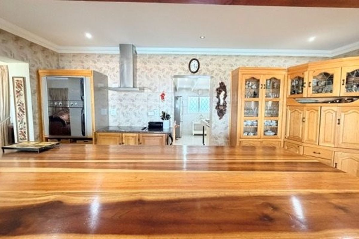 A spacious kitchen featuring extensive timber cabinetry, a large wooden island countertop, built-in oven, and a stainless steel extractor fan.