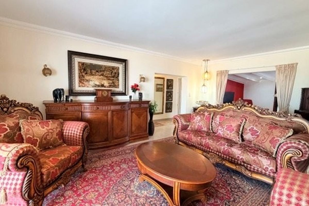 A spacious living room featuring decorative crown molding, wall-mounted light fixtures, and an open transition to an adjacent room.