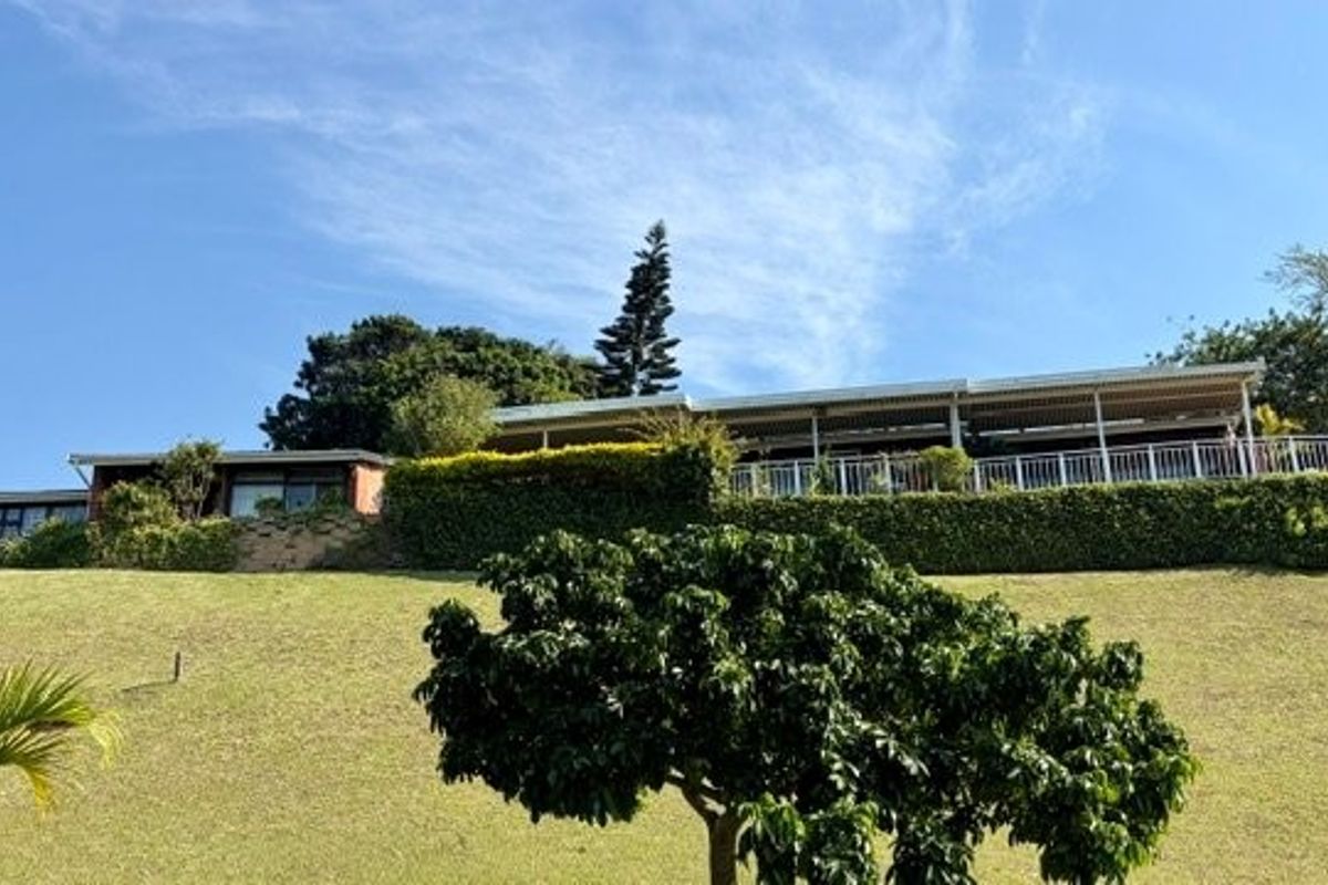 A rear view of the townhouse featuring an elevated patio with metal balustrades, overlooking a well-maintained sloping garden and retaining wall.
