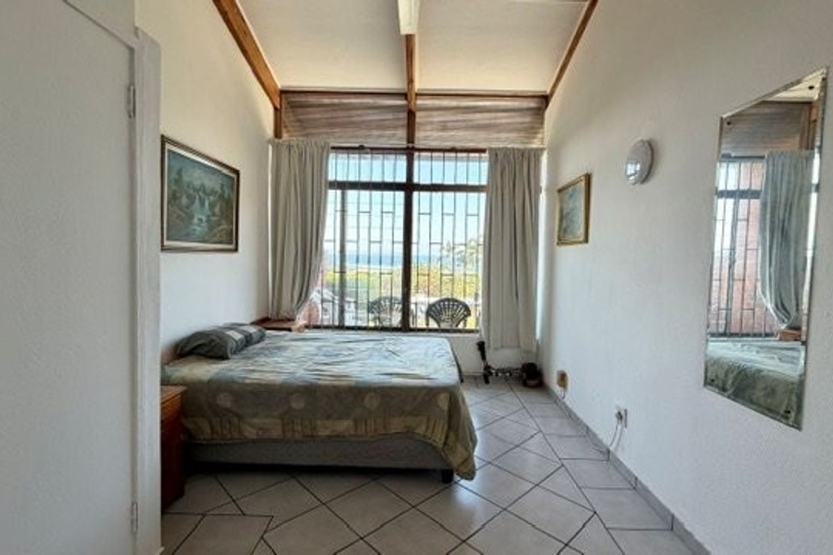 A bedroom featuring vaulted ceilings with exposed timber beams, tiled flooring, and large windows with security bars offering natural light.