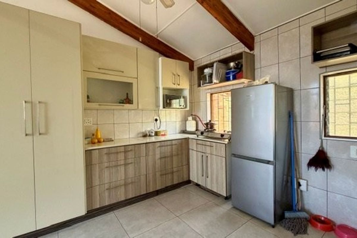Functional kitchen featuring built-in cabinetry, tiled backsplash, and exposed timber ceiling beams, offering a practical layout with ample storage space.