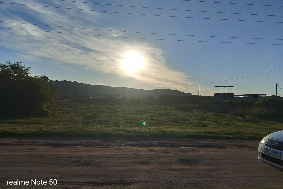 A view of a vacant residential plot from the street, featuring open land with distant mountain views and overhead power lines.