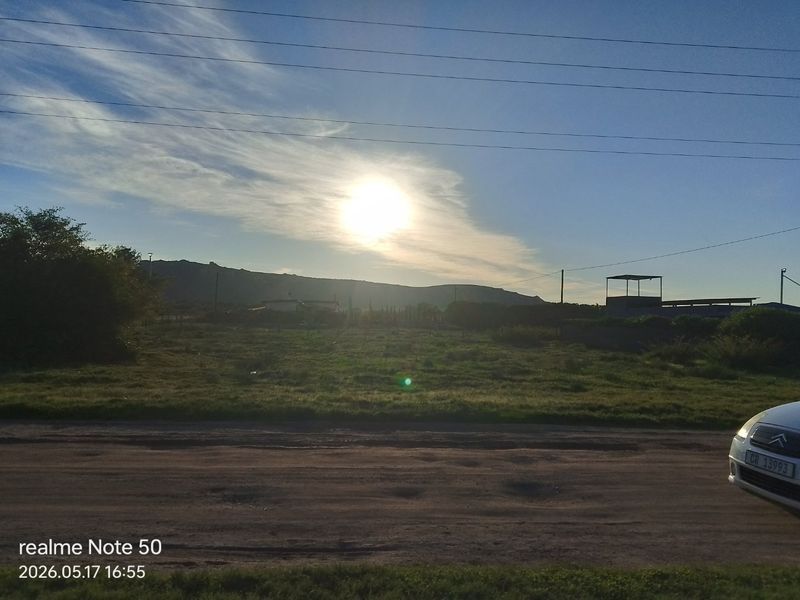 A view of a vacant residential plot from the street, featuring open land with distant mountain views and overhead power lines.