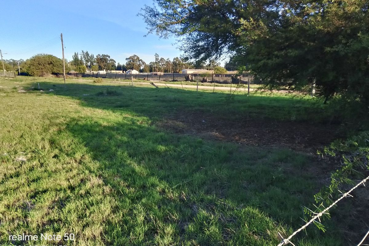 A view of a vacant residential plot featuring grassy terrain, mature trees, and perimeter wire fencing.