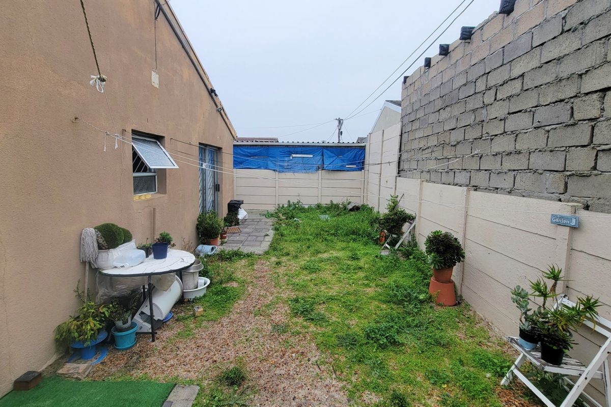 Rear exterior area featuring a paved walkway, overgrown lawn, and boundary walls requiring maintenance and landscaping improvements.
