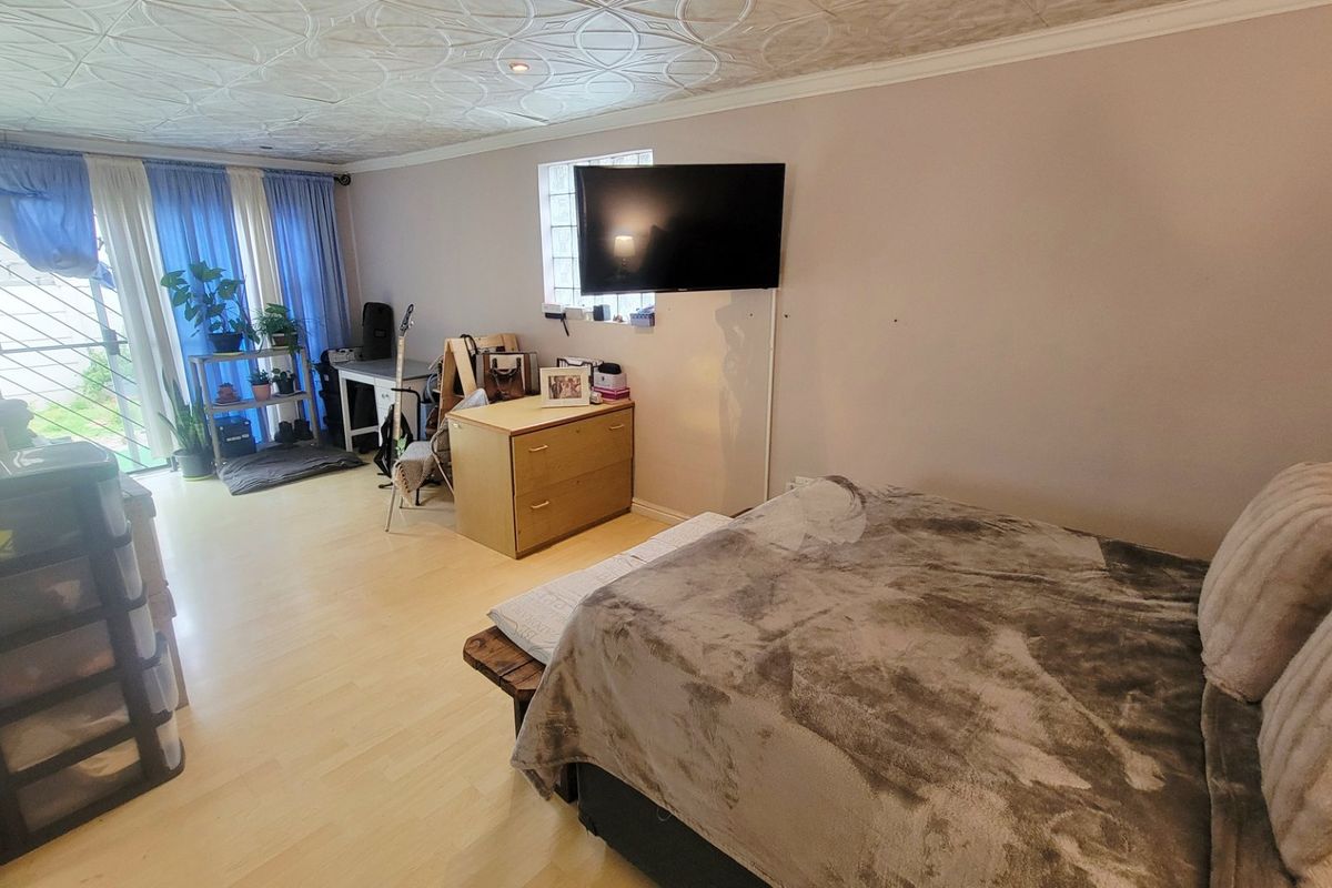A bedroom featuring laminate flooring, decorative ceiling tiles, and a glass block window with access to an exterior security gate.