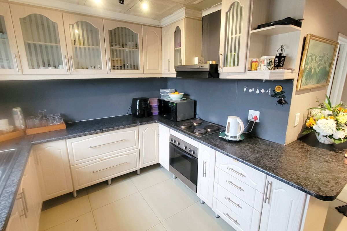 A functional kitchen featuring light-toned cabinetry, dark laminate countertops, a built-in oven with electric hob, and tiled flooring.