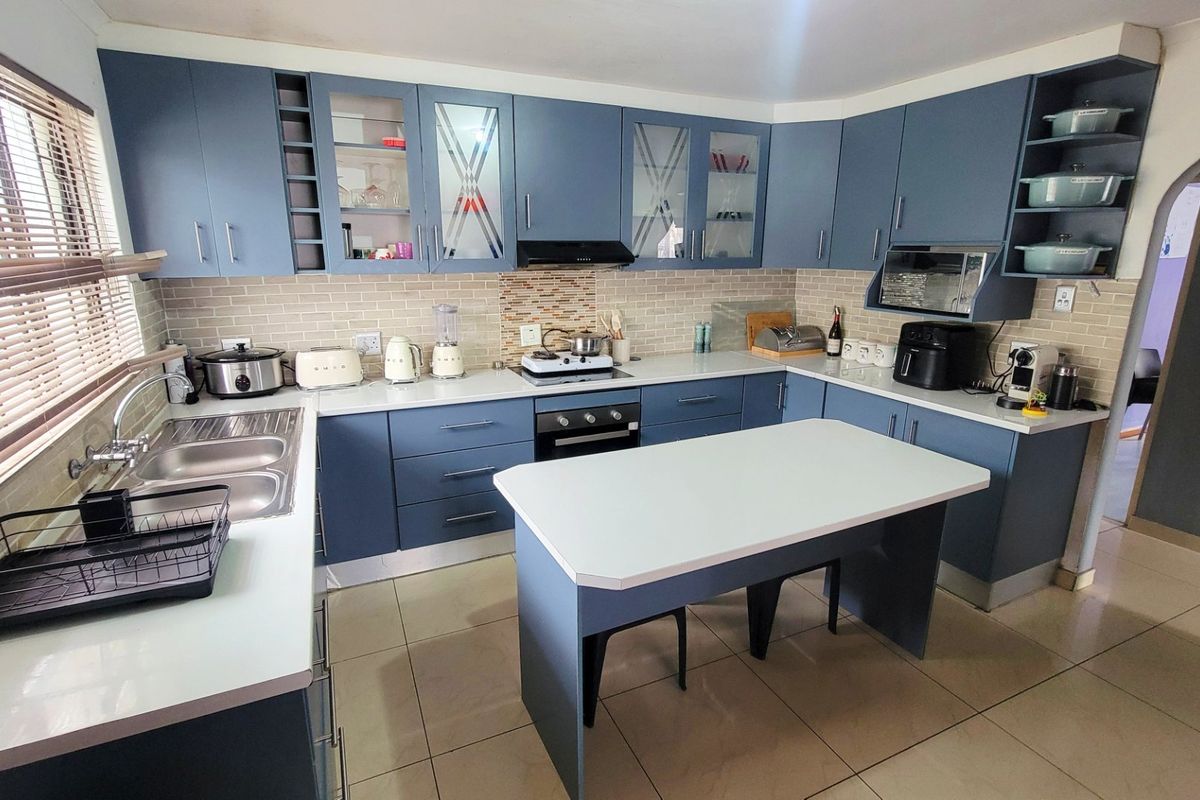 A well-maintained kitchen featuring blue cabinetry, a central island, tiled backsplash, and integrated appliances including an oven and hob.