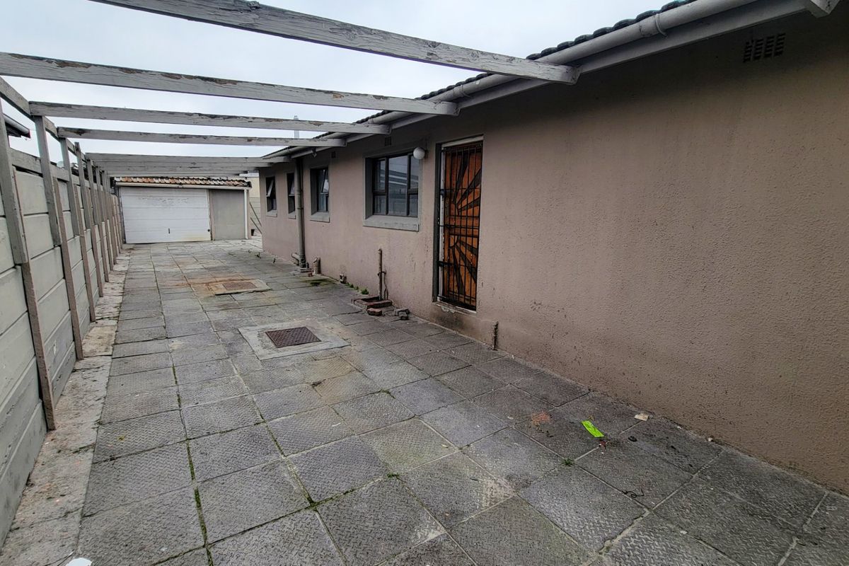 Rear exterior area featuring a paved driveway, timber pergola structure, and access to a detached garage with security gate entry.
