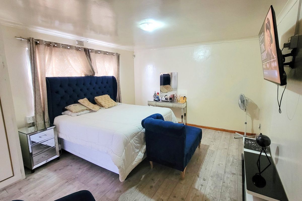 A spacious bedroom featuring laminate flooring, built-in wardrobe storage, and a wall-mounted television setup.