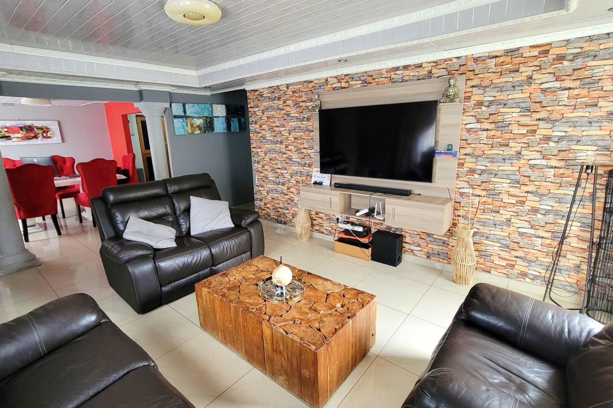 Spacious living room featuring a stone veneer accent wall with a built-in media unit, tiled flooring, and decorative columns leading to the dining area.