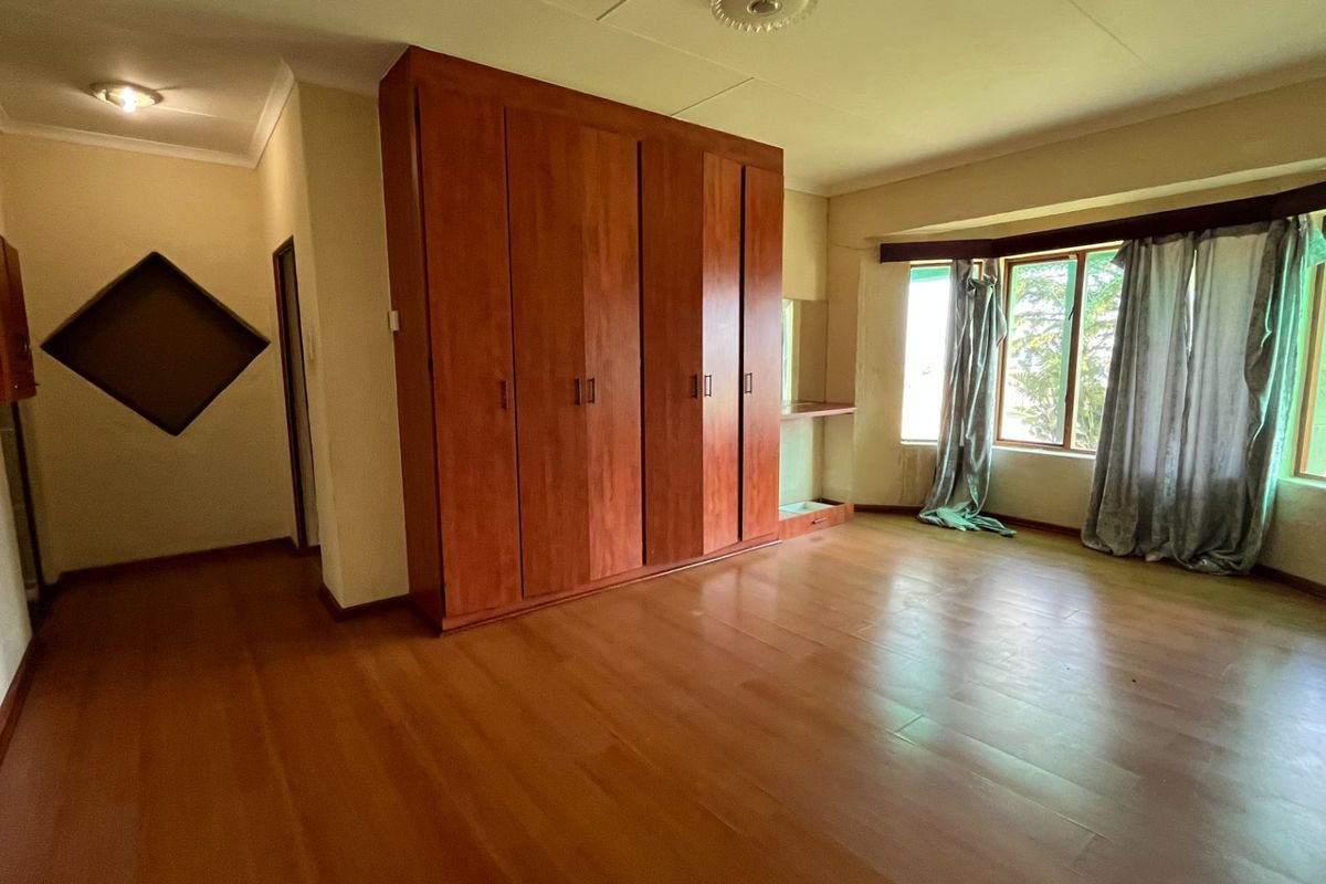 Spacious bedroom featuring laminate flooring, a large built-in wooden wardrobe, and a bay window that provides natural light.