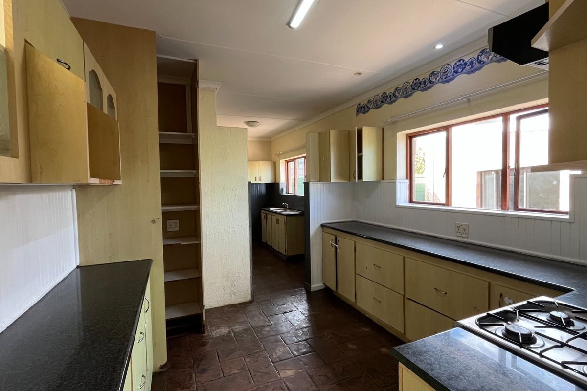 A spacious, dated kitchen featuring extensive built-in cabinetry, dark laminate countertops, a gas hob, and tiled flooring, offering significant potential for modernization.