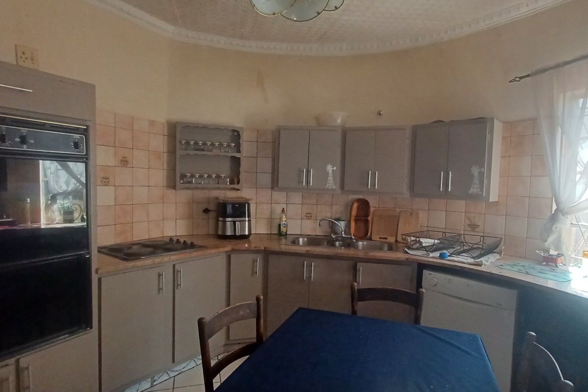 A functional kitchen featuring built-in oven, electric hob, double sink, and ample cabinetry with tiled splashbacks and classic ceiling cornice detailing.