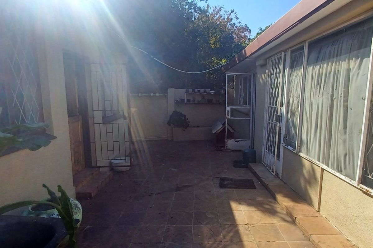 A rear exterior view of the property featuring a tiled patio area, security gates, and boundary walling.