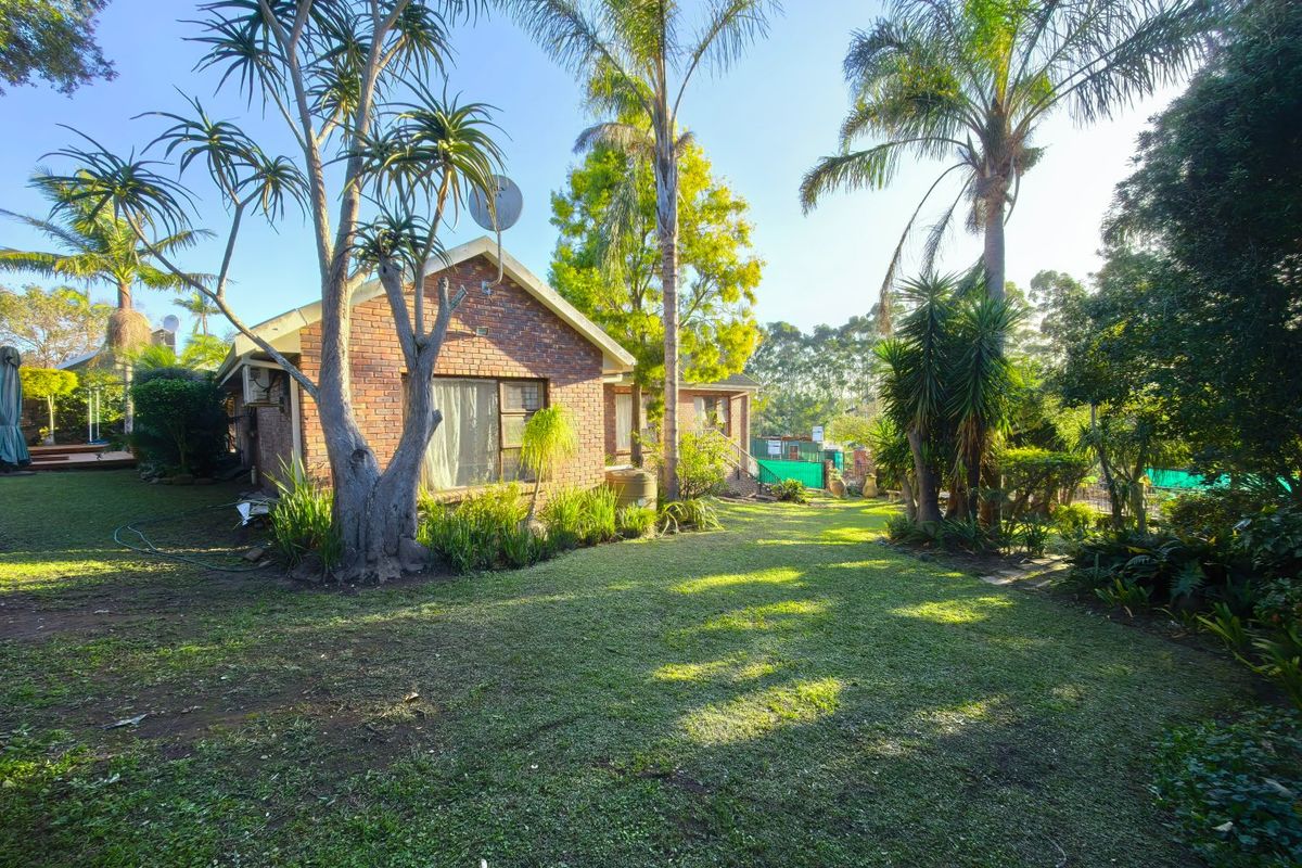 A view of the rear brick facade of the house, featuring a spacious garden with mature trees and established landscaping.