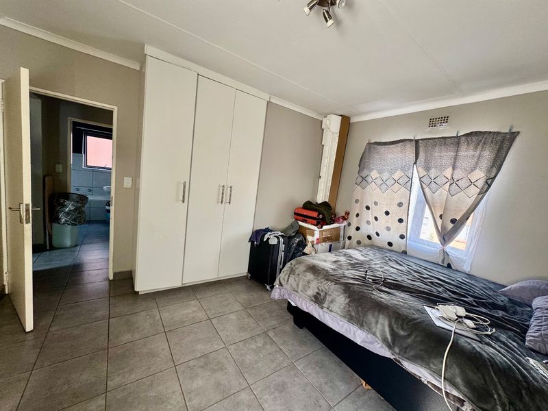 A bedroom featuring built-in cupboards, tiled flooring, and an adjoining bathroom, offering a functional layout with neutral wall finishes.
