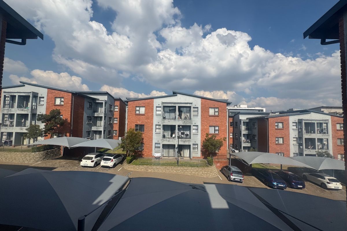 View of a multi-story apartment complex featuring face-brick facades, private balconies, and covered parking bays within a residential estate.