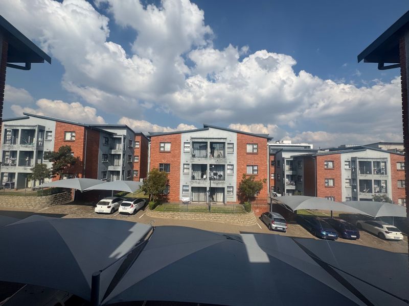 View of a multi-story apartment complex featuring face-brick facades, private balconies, and covered parking bays within a residential estate.