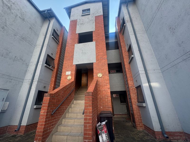Exterior view of an apartment building entrance featuring a brick facade, central staircase, and paved access area.