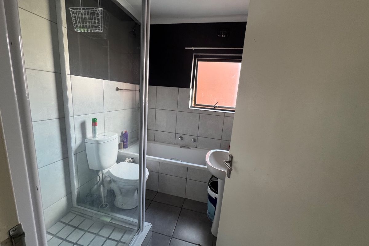 A functional bathroom featuring a separate shower enclosure, bathtub, pedestal basin, and toilet with neutral wall and floor tiling.
