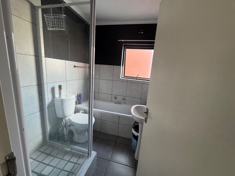 A functional bathroom featuring a separate shower enclosure, bathtub, pedestal basin, and toilet with neutral wall and floor tiling.