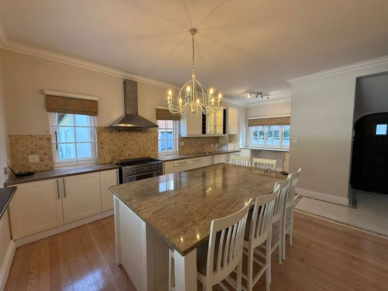 Spacious kitchen featuring a large granite-topped island, stainless steel extractor fan, gas stove, and ample built-in cabinetry with hardwood flooring.
