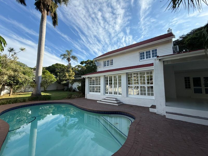 Rear view of the property featuring a swimming pool, brick paved patio area, and white weatherboard exterior with classic multi-pane windows and french doors.