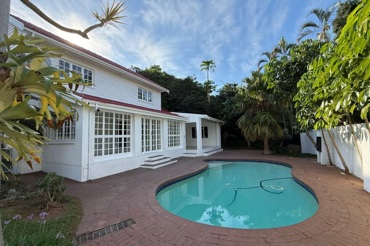 Rear view of the property featuring a swimming pool, brick paved patio area, and white exterior facade with multi-pane windows and doors.