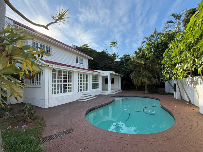 Rear view of the property featuring a swimming pool, brick paved patio area, and white exterior facade with multi-pane windows and doors.