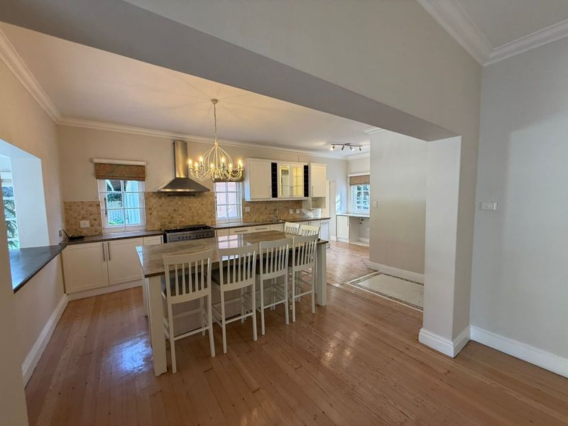 Spacious open-plan kitchen featuring a central island, modern cabinetry, gas hob with extractor, and polished hardwood flooring, flowing into an adjacent prep area.