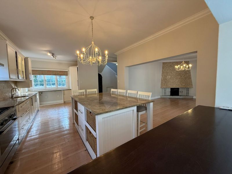 Spacious open-plan kitchen and living area featuring a large central island with granite countertops, hardwood flooring, and a distinctive stone-clad fireplace.