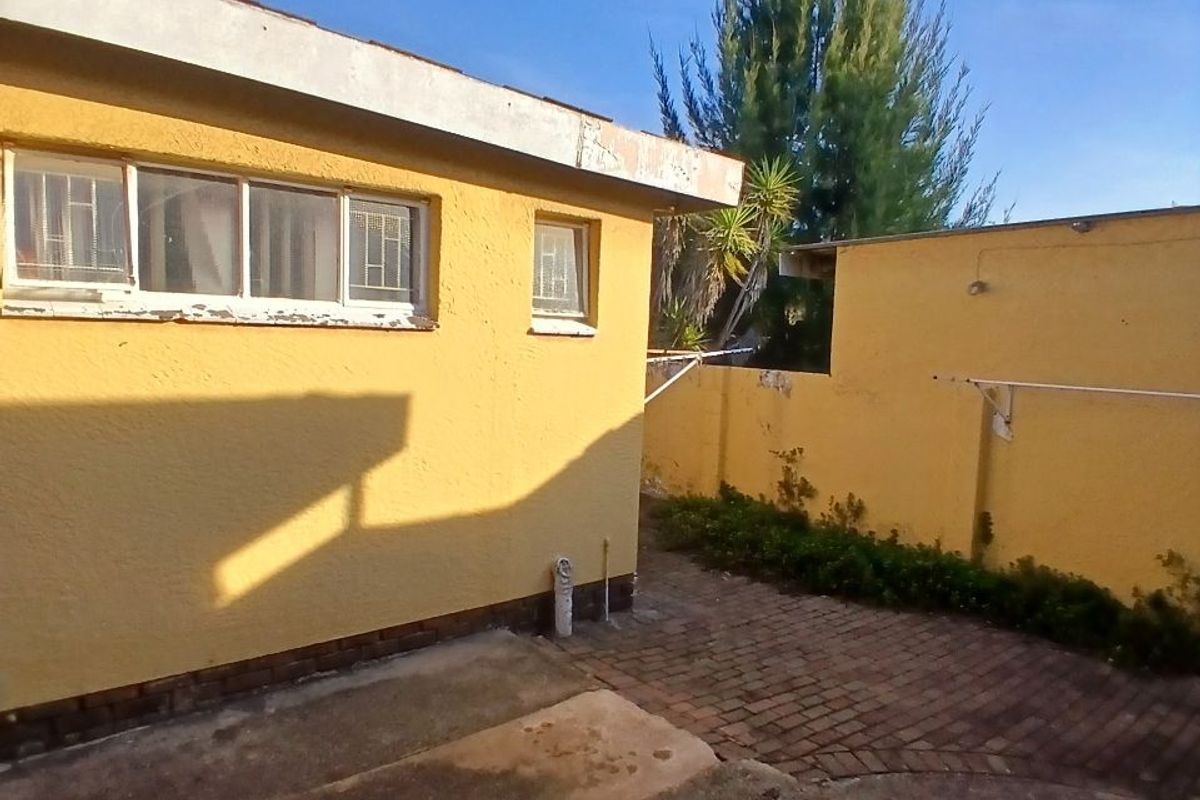 Rear exterior view of the property featuring a paved courtyard, boundary wall, and yellow painted exterior walls with visible signs of weathering.