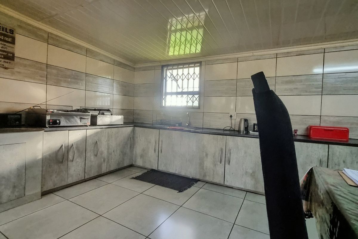 A functional kitchen featuring tiled walls, built-in cabinetry, a stainless steel sink, and a security-grilled window.