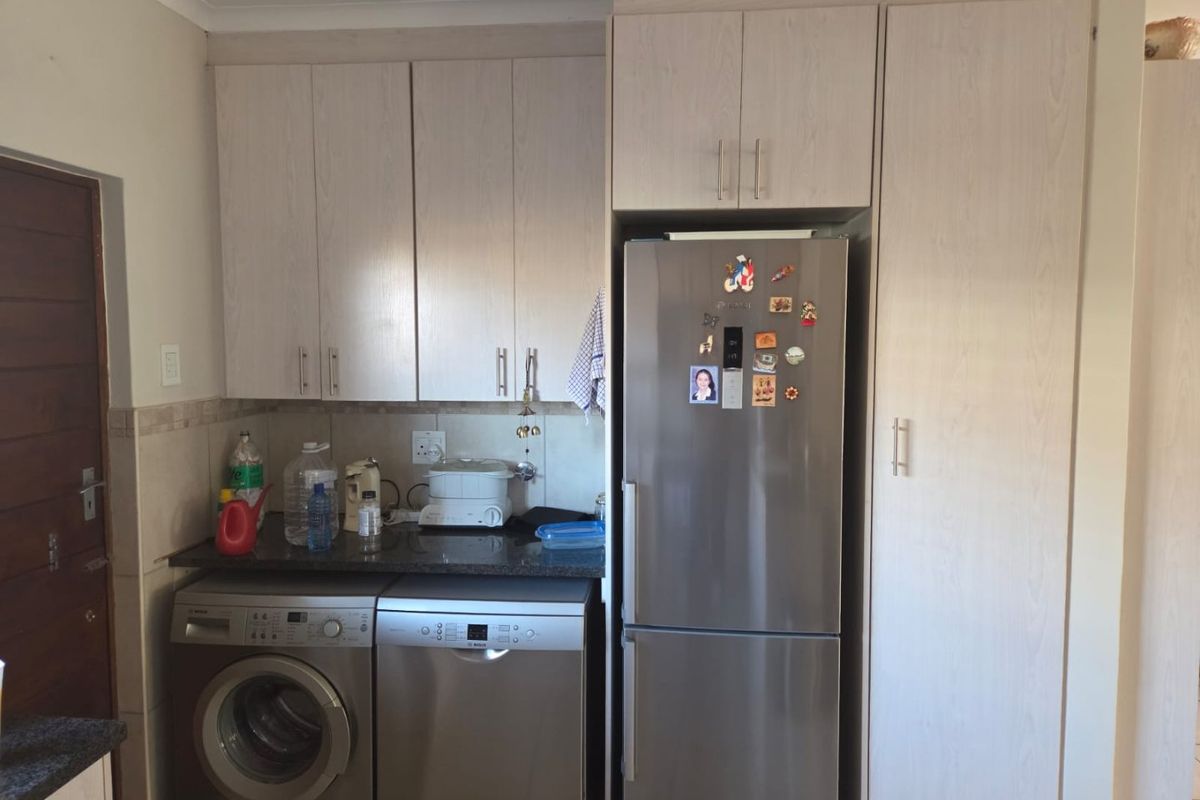 A functional kitchen area featuring light wood-finish cabinetry, granite countertops, and dedicated spaces for laundry and kitchen appliances.