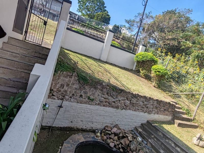Rear garden area featuring a stone retaining wall, concrete staircase, and a small ornamental pond set within a fenced yard.