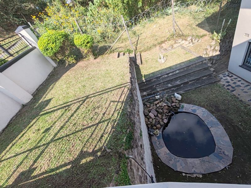 A tiered backyard garden featuring a stone water feature, concrete stairs, and a retaining wall, enclosed by a security fence.